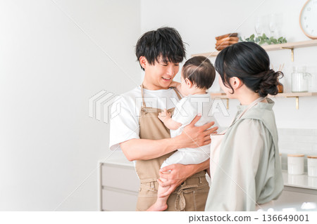 一對穿著圍裙的夫婦抱著嬰兒在廚房裡,一家人 一對穿著圍裙的夫婦抱著嬰兒在廚房裡,一家人 136649001