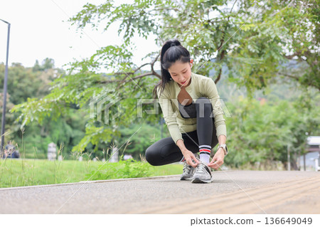 Asian woman in sportswear sitting and tying sneaker's shoelace before running exercising by the road 136649049