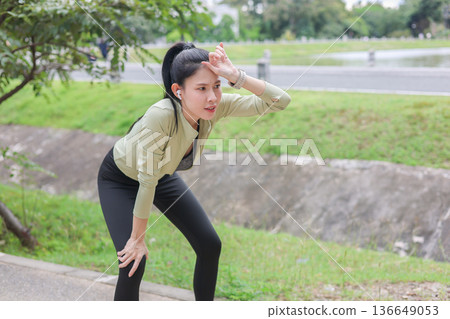 Tired asian woman in green sportswear hand on knee and wiping sweat after running exercising in park Tired asian woman in green sportswear hand on knee and wiping sweat after running exercising in park 136649053