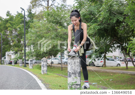 Asian woman in sportswear tying sneaker's shoelace on pillar before running exercising by the road 136649058