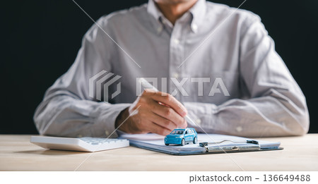 Person prepares to sign auto loan contract, document for car purchase, lease agreement at dealership, finance insurance forms, vehicle sale transaction paperwork, blue car model, calculator on desk Person prepares to sign auto loan contract, document for car purchase, lease agreement at dealership, finance insurance forms, vehicle sale transaction paperwork, blue car model, calculator on desk 136649488