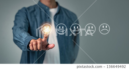 Customer experience relies on consistent feedback, as seen when a man selects the best smiley face icon to give his evaluation, which offers vital feedback on service quality and satisfaction Customer experience relies on consistent feedback, as seen when a man selects the best smiley face icon to give his evaluation, which offers vital feedback on service quality and satisfaction 136649492