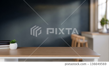 Books and potted plant on wooden table across blue wall and stool chair with sunlight through window 136649569