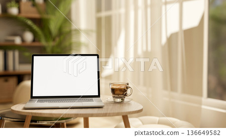 White screen laptop and coffee cup on wooden table at living room floor and sunlight through window. 136649582