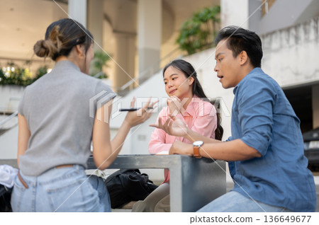 Man and woman asian student friends talking while working on group project at table in a university. Man and woman asian student friends talking while working on group project at table in a university. 136649677