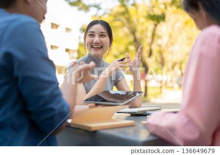 Asian woman student hold pen listening to friends talking as working on group project in university. Asian woman student hold pen listening to friends talking as working on group project in university. 136649679