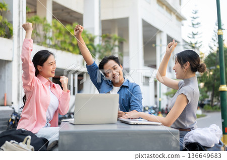 Asian woman student raising a fist with man and friend while working on group project in university. Asian woman student raising a fist with man and friend while working on group project in university. 136649683