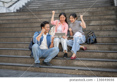 Asian man woman student looking at tablet raising fist in excited as sitting on stairs in university Asian man woman student looking at tablet raising fist in excited as sitting on stairs in university 136649698