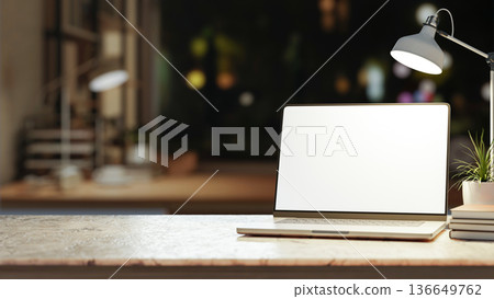 White screen laptop and book under lamp on marble counter table across window in dim room at night. White screen laptop and book under lamp on marble counter table across window in dim room at night. 136649762