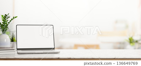 White screen laptop and books with pot plants vase on marble counter table in a blurred bright room 136649769