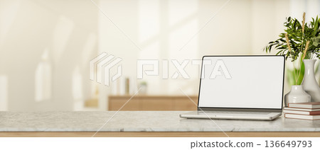 Blank screen laptop and books aside plant vase on marble counter table in a white room with sunlight Blank screen laptop and books aside plant vase on marble counter table in a white room with sunlight 136649793