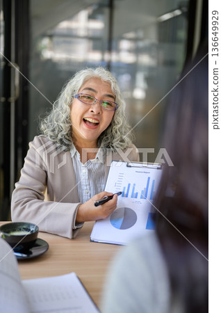 Old asian businesswoman holding clipboard pointing pen talking to employee office worker in company/ Old asian businesswoman holding clipboard pointing pen talking to employee office worker in company/ 136649929