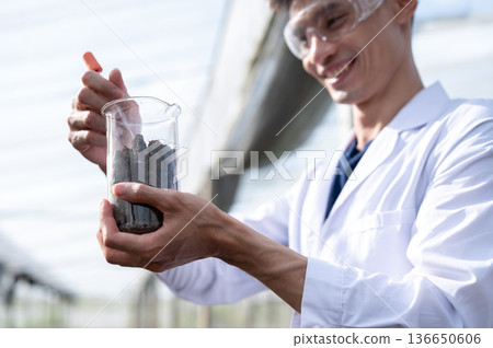 Glasses asian agricultural scientist man holding beaker testing on planting soils in greenhouse farm Glasses asian agricultural scientist man holding beaker testing on planting soils in greenhouse farm 136650606