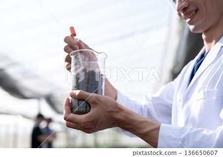 Blurred asian agricultural scientist man holding beaker testing on planting soils in greenhouse farm Blurred asian agricultural scientist man holding beaker testing on planting soils in greenhouse farm 136650607