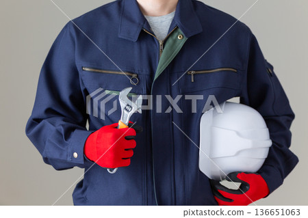 一位身穿工作服的中年男性商人，手持工具和頭盔。 136651063