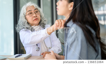 Old asian woman doctor looking or checking on young patient neck sitting at table in diagnosis room. 136651064