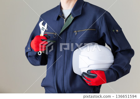 一位身穿工作服的中年男性商人，手持工具和頭盔。 136651594