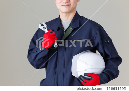 一位身穿工作服的中年男性商人，手持工具和頭盔。 136651595