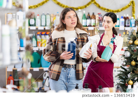 Young saleswoman offering spray cleaner to girl in store decorated for Xmas 136653419