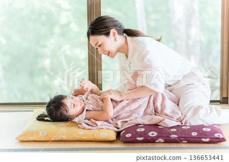 一位微笑的母親在日式高架房間哄女兒睡覺。 136653441