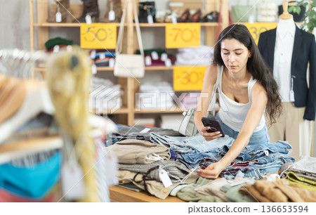 Young woman scans QR code and label of trousers or pants using mobile phone camera Young woman scans QR code and label of trousers or pants using mobile phone camera 136653594