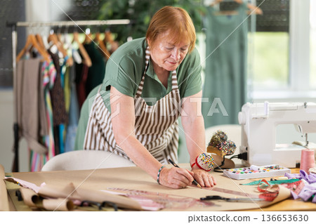 Woman dressmaker drawing pattern on paper in workshop 136653630