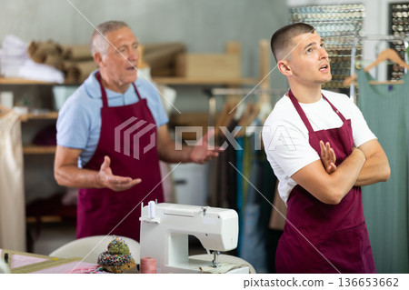 Elderly man scolding young man in sewing workshop Elderly man scolding young man in sewing workshop 136653662