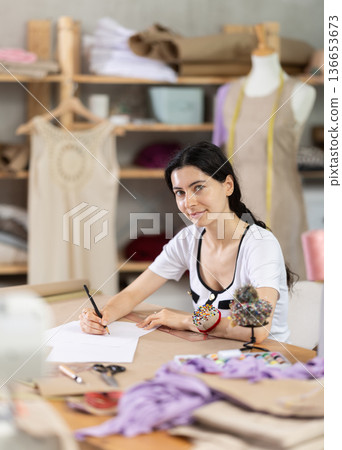 Female tailor drawing sketches of custom garment by hand in studio Female tailor drawing sketches of custom garment by hand in studio 136653673