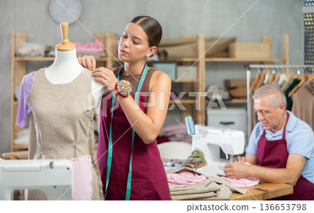 Young woman working with mannequin, elderly man sewing 136653798