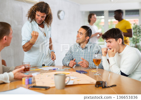 Group of enthusiastic men playing board game sitting around table 136653836