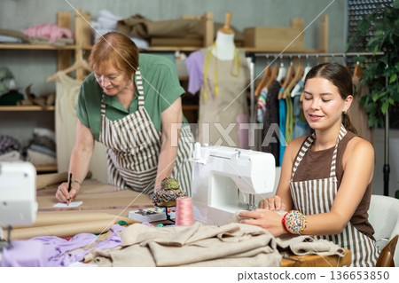 Mature dressmaker drawing patterns next to young assistant Mature dressmaker drawing patterns next to young assistant 136653850