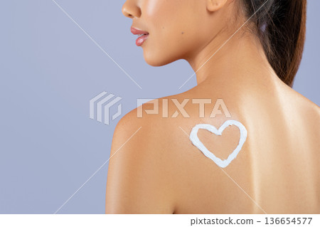 A woman stands with her back to the viewer, showing a heart shape created with sunscreen on her skin. The background is simple and the scene suggests a focus on sun protection. A woman stands with her back to the viewer, showing a heart shape created with sunscreen on her skin. The background is simple and the scene suggests a focus on sun protection. 136654577
