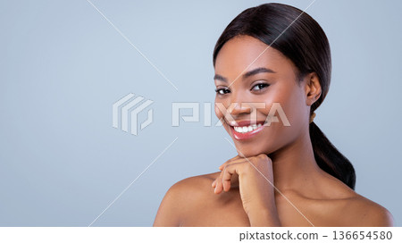 A woman is smiling at the camera while resting her chin on her hand. She has long dark hair and a pleasant expression. The background is light and plain. The moment captures confidence. 136654580