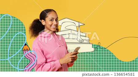 A happy African American teen girl is texting on her cellphone. She is wearing a pink hoodie and smiling. The backdrop is bright yellow, adding to the cheerful mood of the scene. A happy African American teen girl is texting on her cellphone. She is wearing a pink hoodie and smiling. The backdrop is bright yellow, adding to the cheerful mood of the scene. 136654581