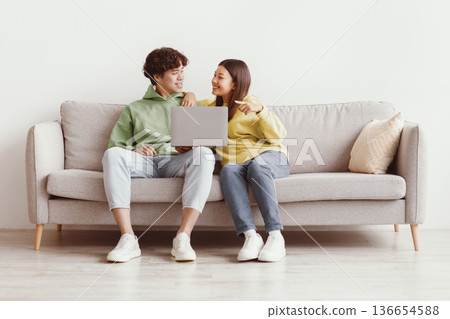 Millennial Asian couple using laptop computer together, sitting on sofa at home, free space. Loving young man and woman having online conference with friends, video chatting with family Millennial Asian couple using laptop computer together, sitting on sofa at home, free space. Loving young man and woman having online conference with friends, video chatting with family 136654588