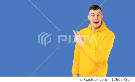 Amazed young caucasian man pointing at copy space for your text or advertisement over blue studio background, showing exciting deal, panorama Amazed young caucasian man pointing at copy space for your text or advertisement over blue studio background, showing exciting deal, panorama 136654594
