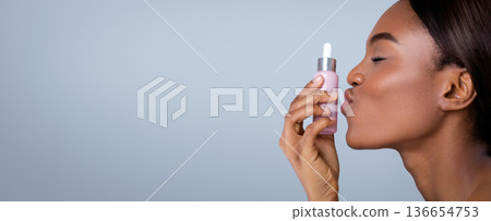 A woman holds a skincare serum bottle close to her face. She gently kisses the bottle with her eyes closed, showing a moment of self-care. The background is simple and light. A woman holds a skincare serum bottle close to her face. She gently kisses the bottle with her eyes closed, showing a moment of self-care. The background is simple and light. 136654753