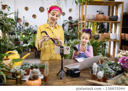 A woman and her daughter are teaching a gardening lesson, using tools and a laptop for their online audience A woman and her daughter are teaching a gardening lesson, using tools and a laptop for their online audience 136655044