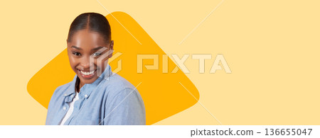 A woman stands facing the camera while smiling. She wears a blue shirt and has her hair neatly styled. The background is a bright yellow color with a geometric shape. A woman stands facing the camera while smiling. She wears a blue shirt and has her hair neatly styled. The background is a bright yellow color with a geometric shape. 136655047