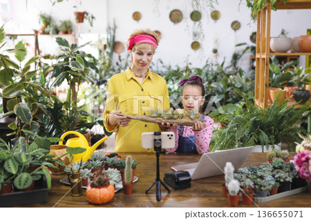 A woman and a girl are holding air plants in a plant shop, filming a video for social media 136655071