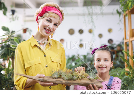 A woman and a young girl smile while holding a piece of driftwood with air plants in a bright, airy space A woman and a young girl smile while holding a piece of driftwood with air plants in a bright, airy space 136655077