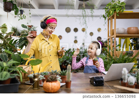 A mother and daughter enjoy music while tending to their plants in a bright, inviting space 136655098