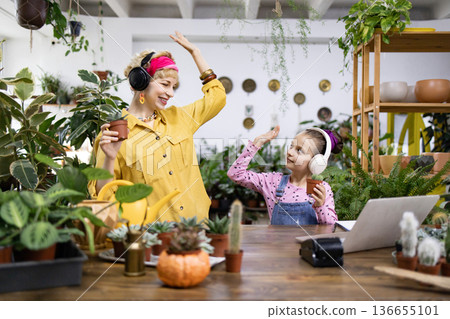A woman and a girl are dancing with plants in a bright, airy greenhouse setting A woman and a girl are dancing with plants in a bright, airy greenhouse setting 136655101