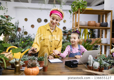 A woman and a girl are working together in a plant shop, surrounded by various plants and succulents A woman and a girl are working together in a plant shop, surrounded by various plants and succulents 136655127