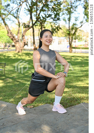 Smiling asian woman in sportswear stretching muscles before exercise on concrete stairs in the park Smiling asian woman in sportswear stretching muscles before exercise on concrete stairs in the park 136655128