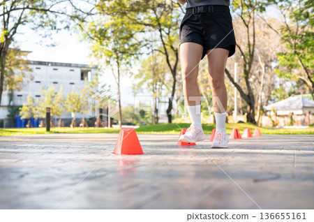 Close up of a woman's legs in sportswear running doing cone drill on pavement in park under sunlight Close up of a woman's legs in sportswear running doing cone drill on pavement in park under sunlight 136655161