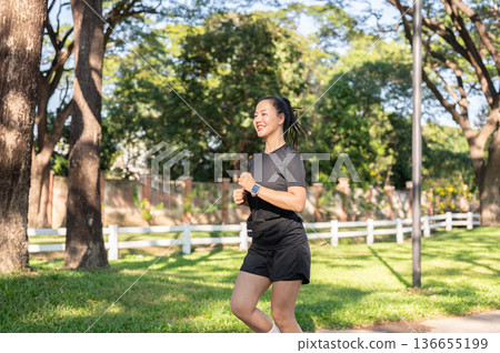 Pretty asian woman in black sportswear exercising by running or jogging in park under the sunlight. 136655199