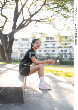 Asian woman in black sportswear holding headphone sitting on concrete stair after exercising in park 136655220