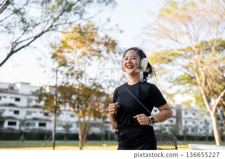 Asian woman in sportswear listening to music in headphone while running jogging exercising in park. Asian woman in sportswear listening to music in headphone while running jogging exercising in park. 136655227