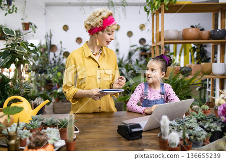 A woman and a girl are discussing something while working on a laptop in a plant shop A woman and a girl are discussing something while working on a laptop in a plant shop 136655239